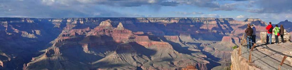 People stand safely behind the guard rail overlooking the Grand Canyon.