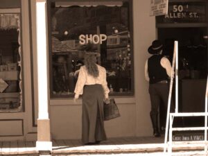 A lady dressed in 1900s clothes looks in a shop windoe
